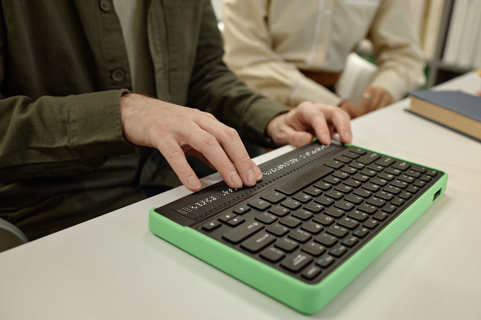 Des mains sur un clavier braille, devant un écran