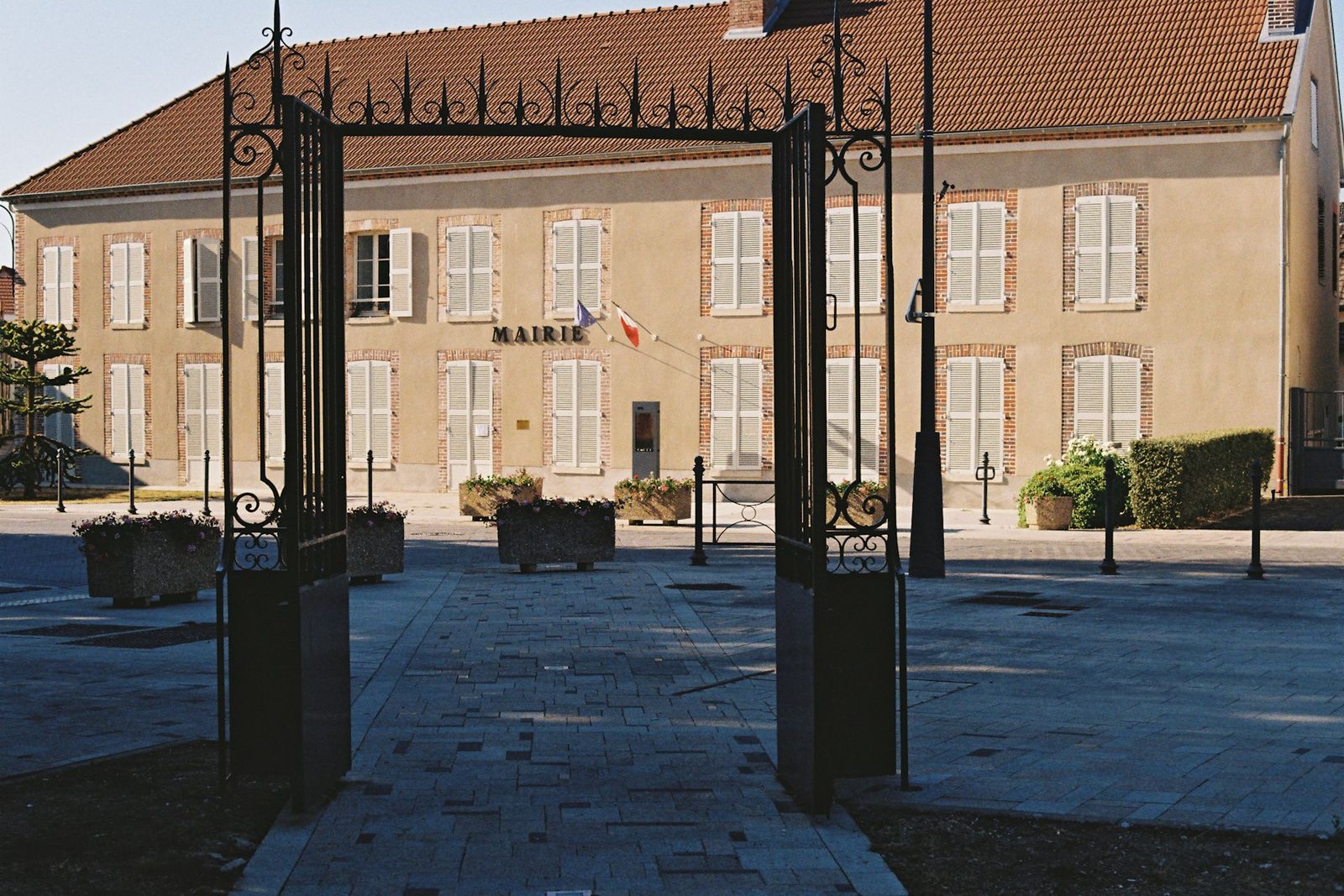 La cour d’une mairie, grille ouverte et drapeaux en façade