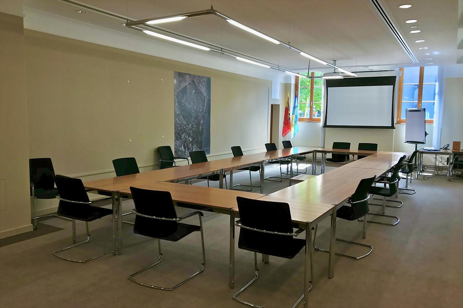 Une salle de conseil municipal, tables en U et écran de projection