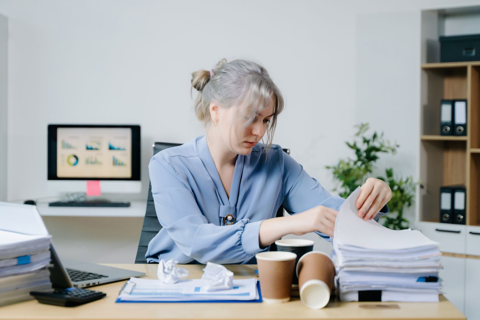 Une employée de bureau classe des dossiers devant son écran